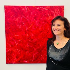 Photo de l'artiste Karine Corbier souriante devant sont monochrome rouge de 1 m par 1 m