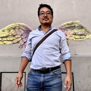 Photo d'un homme dynamique et souriant positionner devant les ailes de la victoire dessinées par Karine Corbier collées sur le mur de la rue
