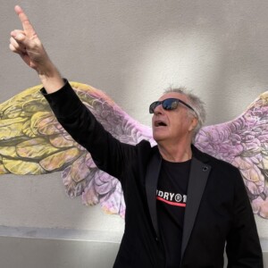 photographie d'un homme montrant le ciel très dynamique posant devant des ailes de la victoire collées sur le mur de la rue lumière magnifique