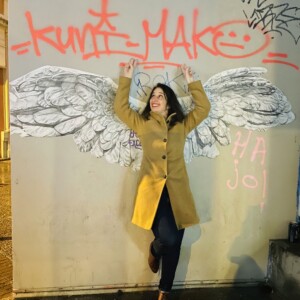 photographie d'une Jeune femme très dynamique et drôle posant devant des ailes de la victoire collées sur le mur de la rue