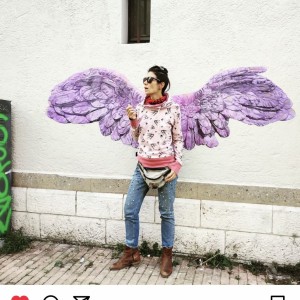 photographie d'une Jeune femme artiste très dynamique posant devant des ailes de la victoire dessinées par Karine Corbier collées sur le mur de la rue Image est une capture d'écran venant d'un compte Instagram de Sarah_Gautier_dessins
