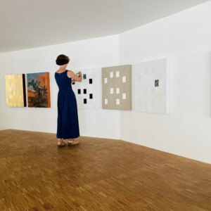 Photo de l'exposition des tableaux de Karine Corbier et Denis Arino où l'on voit une dame en robe bleu marine prendre un des tableaux en photo