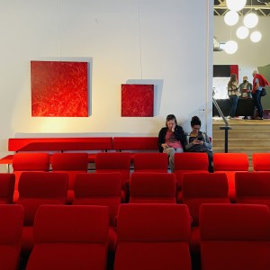 Série de monochrome rouge de différentes tailles dans la salle de spectacle du Moon Shot Lab Les tableaux dialoguent avec le rouge des fauteuils The visiteuse sont assises et regarde leur téléphone