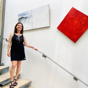 L'artiste Karine Corbier descends des escaliers devant ses œuvres accroché au mur : un diptyque montagne est un monochrome rouge accroché en diagonale