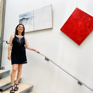 L'artiste Karine Corbier descends des escaliers devant ses œuvres accroché au mur : un diptyque montagne est un monochrome rouge accroché en diagonale